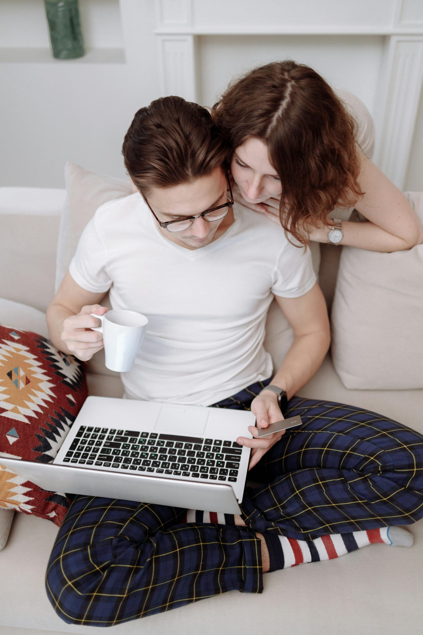 Young couple using a laptop for online shopping on their sofa, holding a credit card.