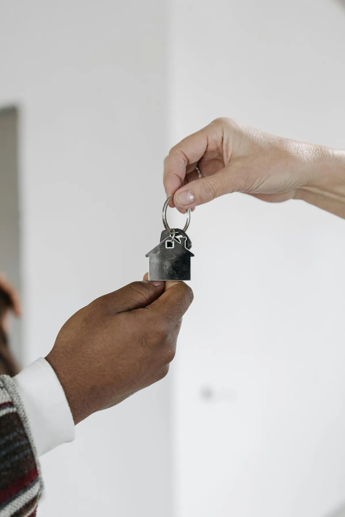 A close-up of two hands exchanging a house-shaped key, symbolizing a home purchase or rental agreement.